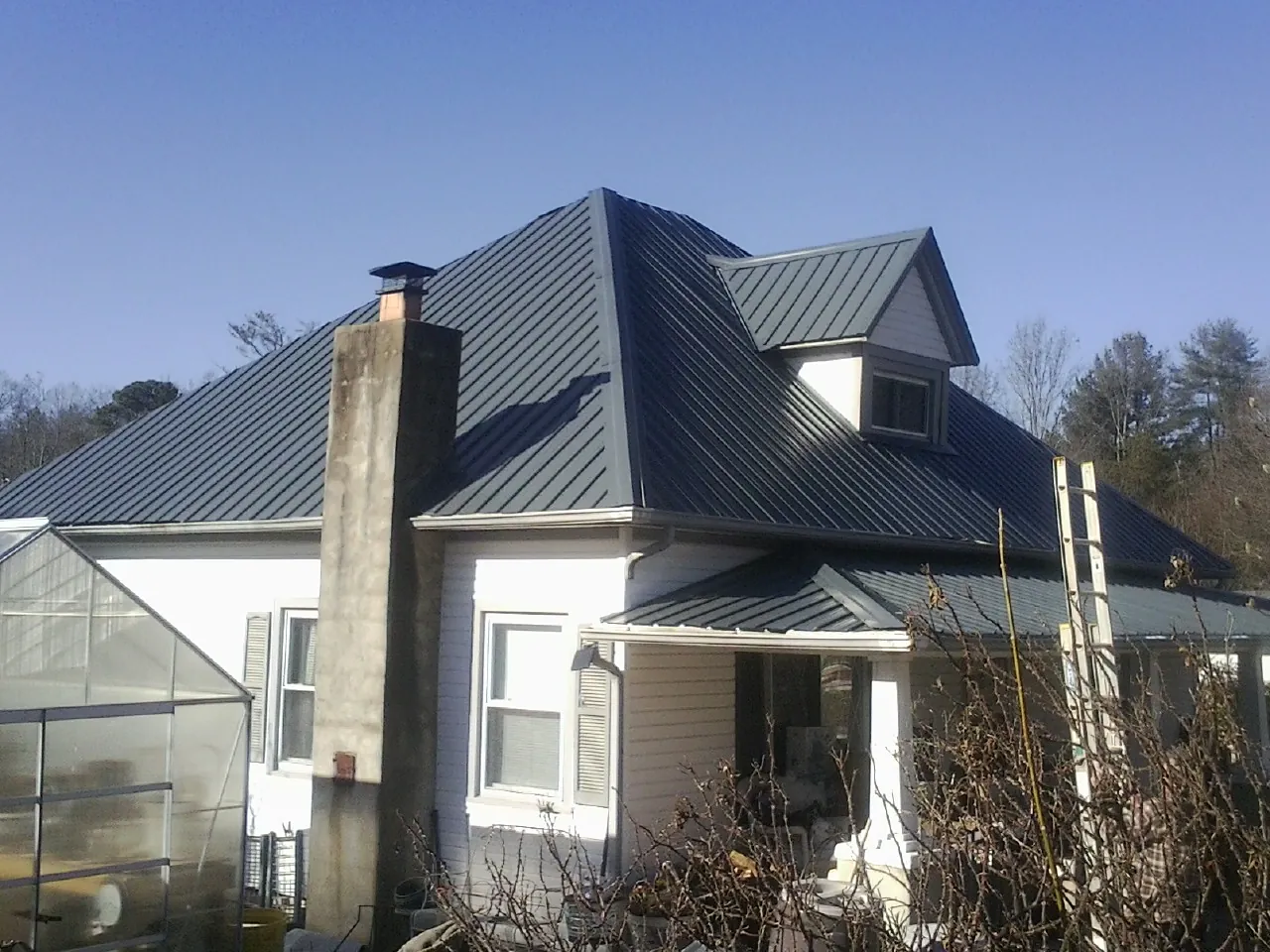 Dark blue standing seam metal roof on a white farmhouse with dormer — Slate & Tile Roof Repair by Roofing Brothers in Willis