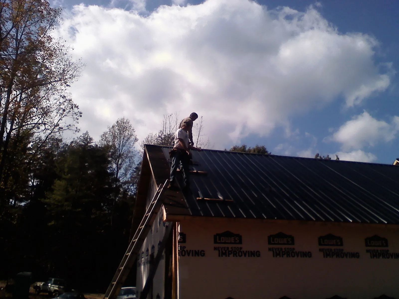 Roofer fastening dark metal panels high against a cloudy sky, from a Roof Inspection job in Willis